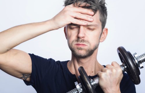 Man lifting weights is tired, has headache from exercise