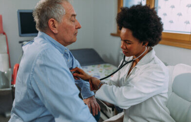 Doctor examining older man, listening to his heart with stethoscope