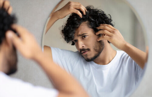 Man examining gray hair, hair loss in mirror