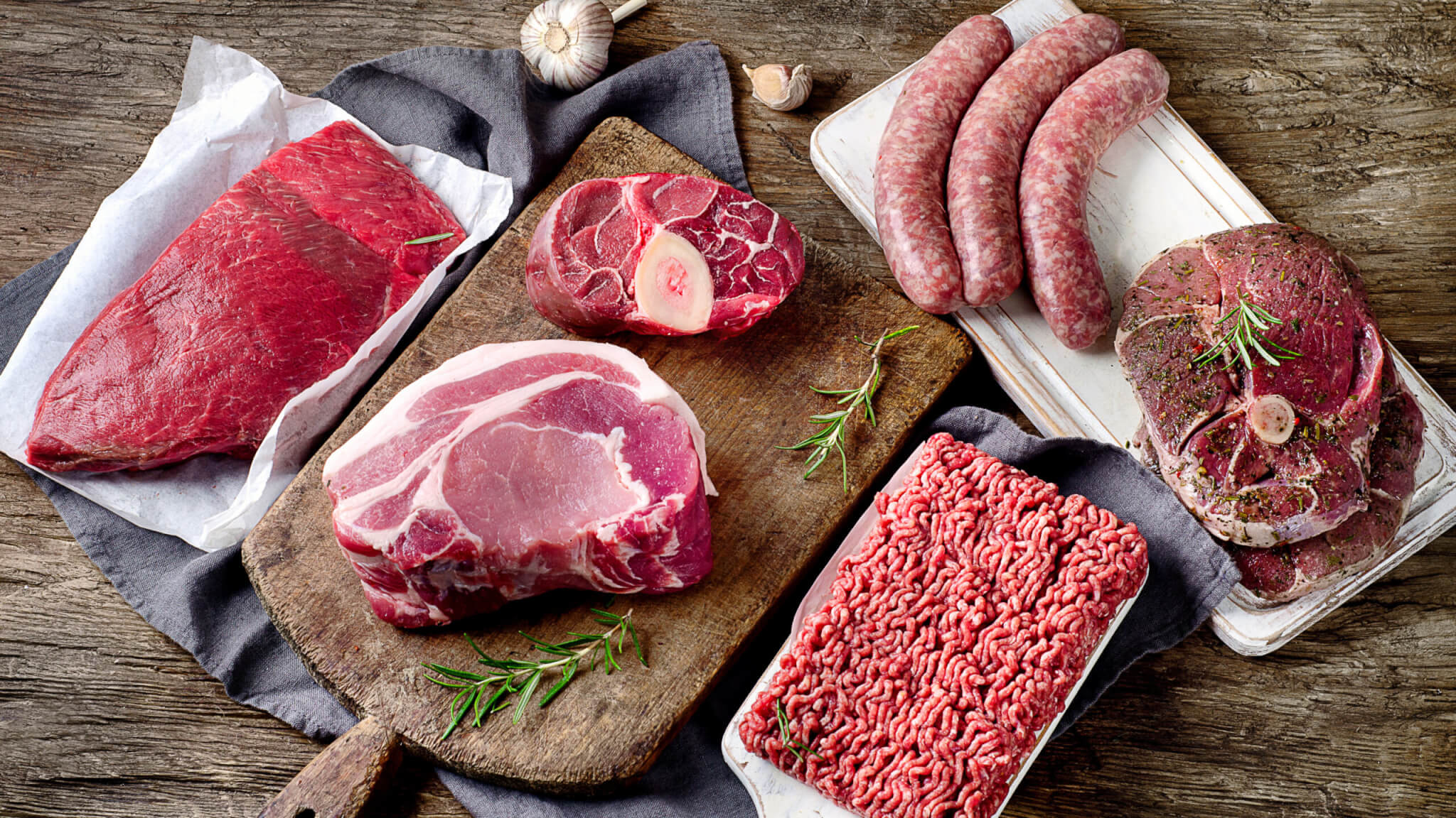 Different types of raw red meat on dark wooden background.