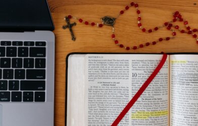 A bible and rosary sits next to a laptop computer
