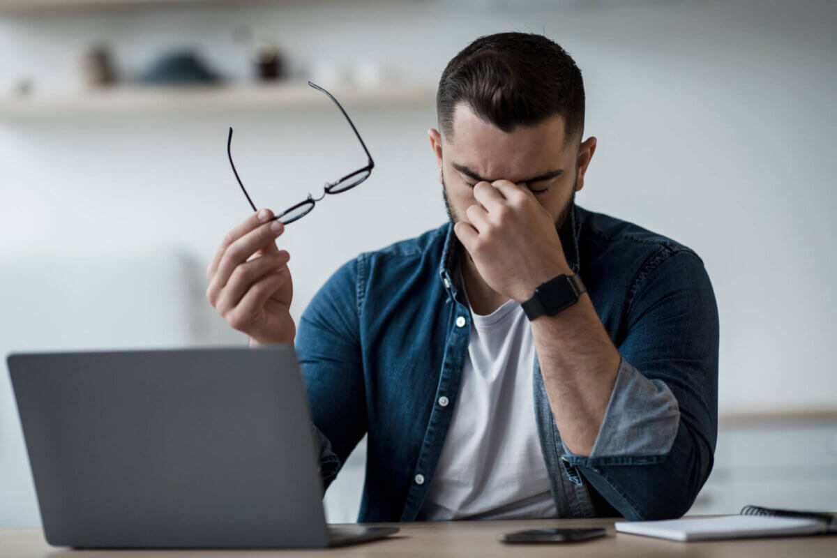 Man rubbing his eyes while working in front of computer, headache, eye strain, stress