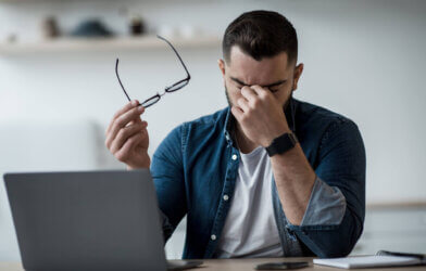 Man rubbing his eyes while working in front of computer, headache, eye strain, stress