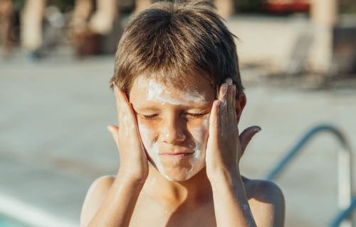 Boy putting sunscreen on his face at the pool