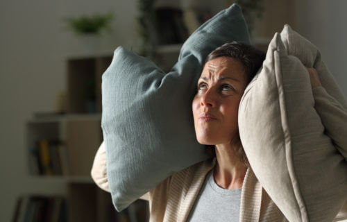 Angry woman covering her ears with pillows because of noisy neighbors
