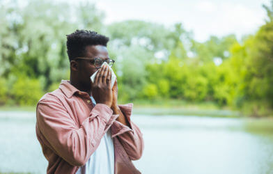 Man blowing his nose, sneezing outside from seasonal allergies