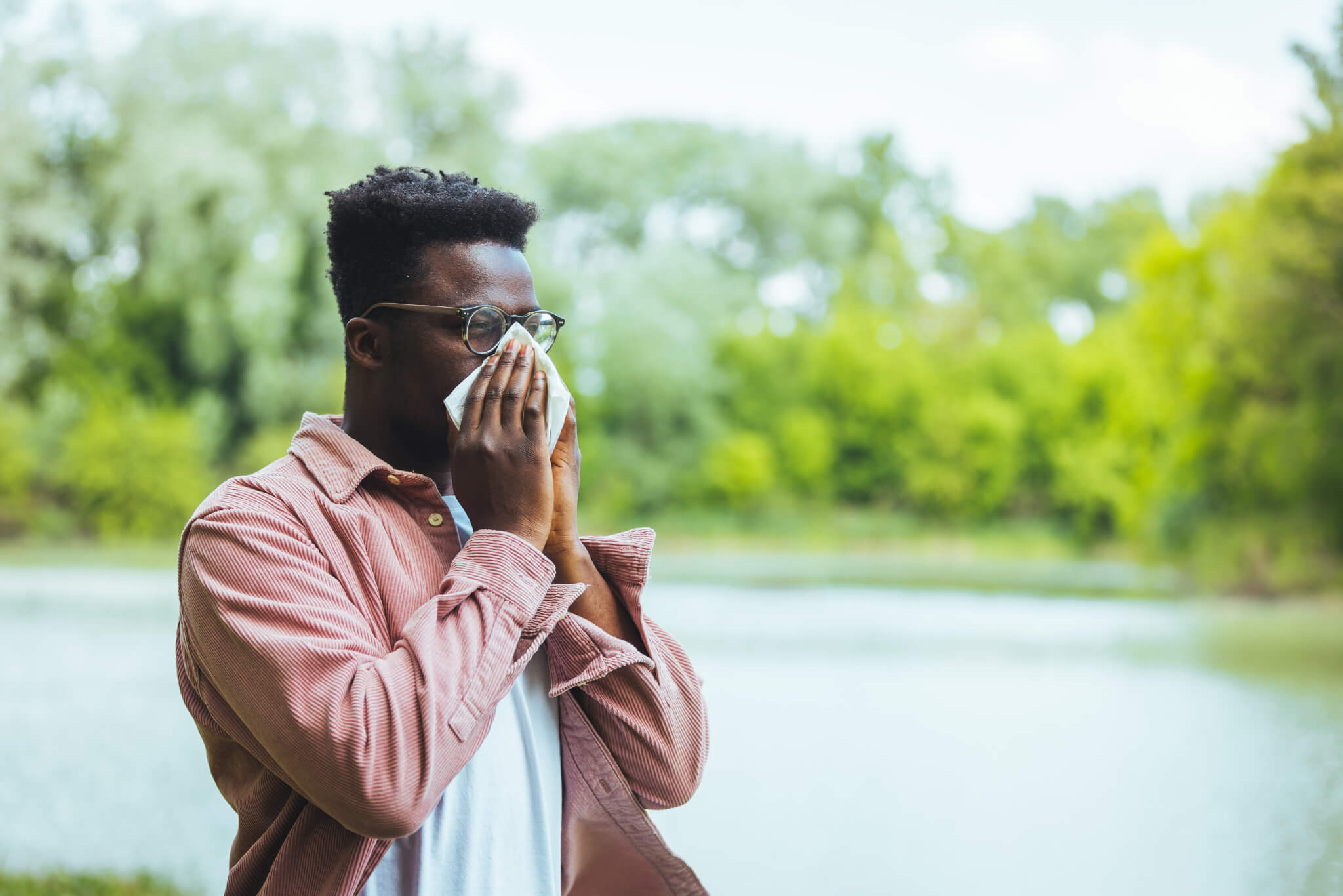 Man blowing his nose, sneezing outside from seasonal allergies
