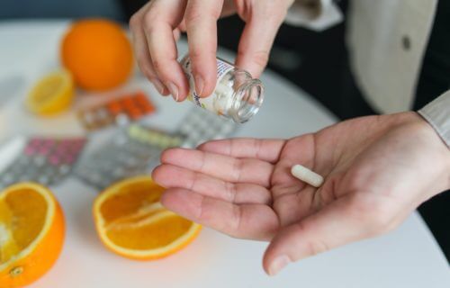Mens multivitamin poured into hand with oranges on table