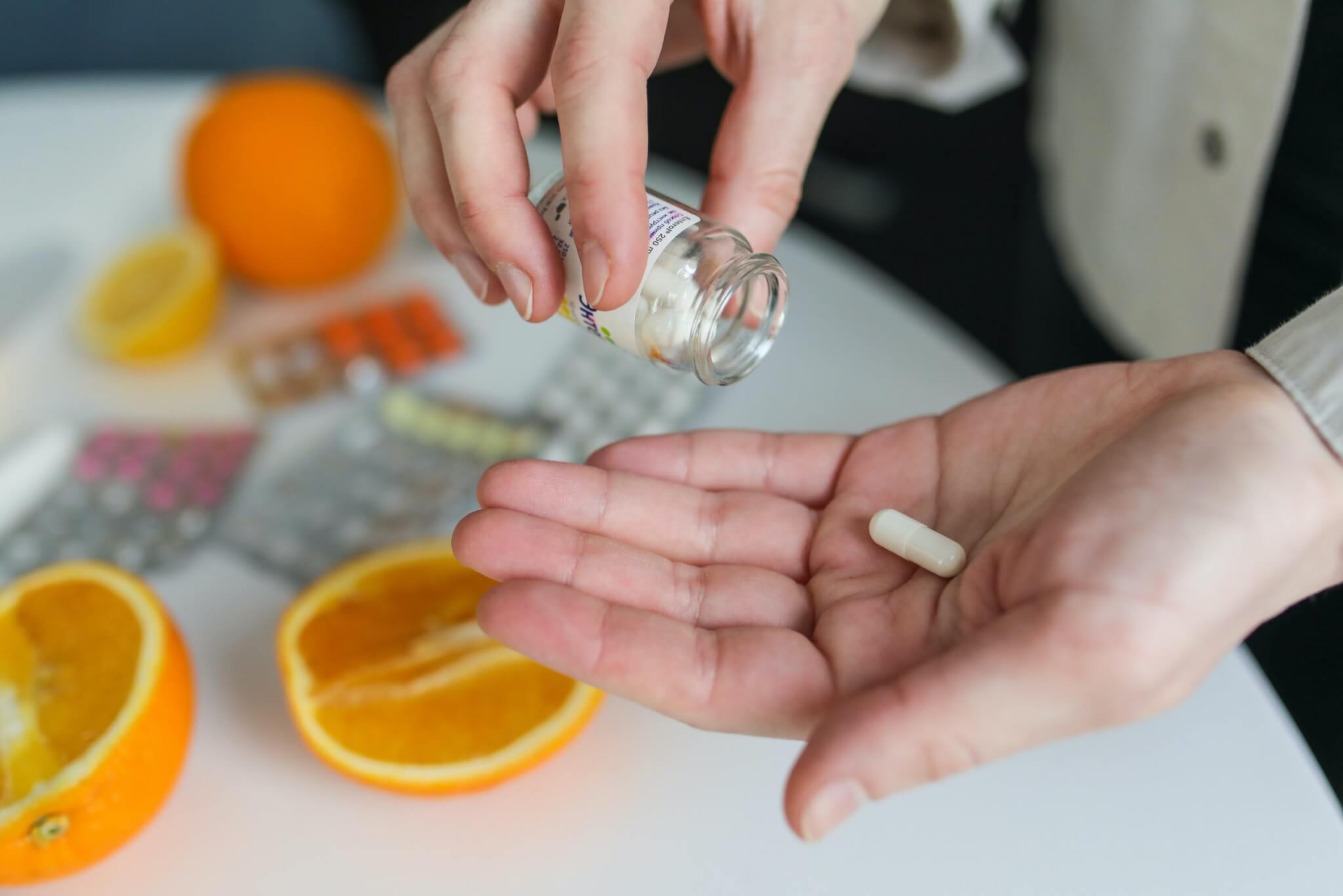 Mens multivitamin poured into hand with oranges on table