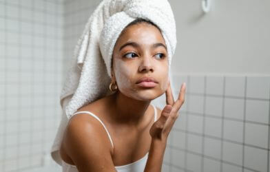 Woman putting face moisturizer cream on after taking a shower.