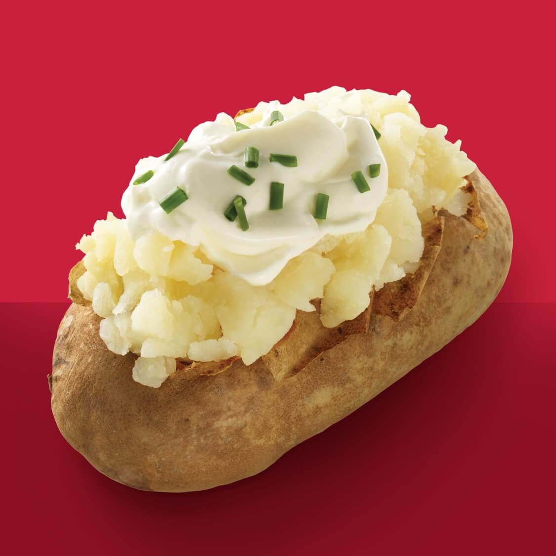 baked potato with butter chives sour cream on red background