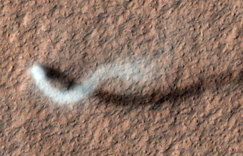 A towering dust devil casts a serpentine shadow over the Martian surface.