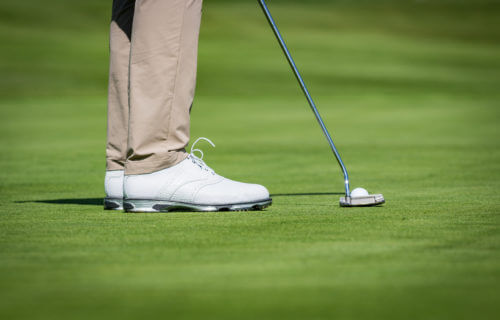 Golfer in white shoes lining up putt