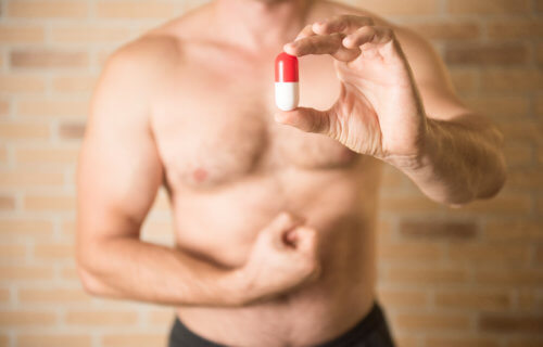 Muscular man holding a testosterone or muscle-building supplement pill