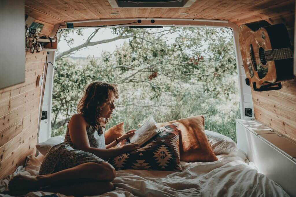 Woman enjoying van life: Lying on bed with trunk opened to wilderness.