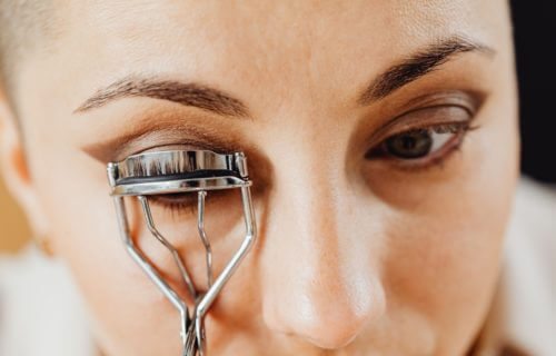 Woman using an eyelash curler while putting on makeup.