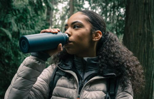 Woman drinking out of a tumbler while walking outside