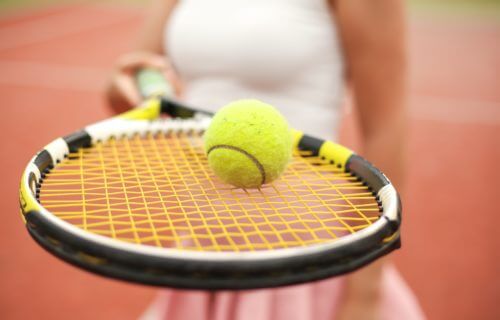 Woman holding tennis racket with ball on top