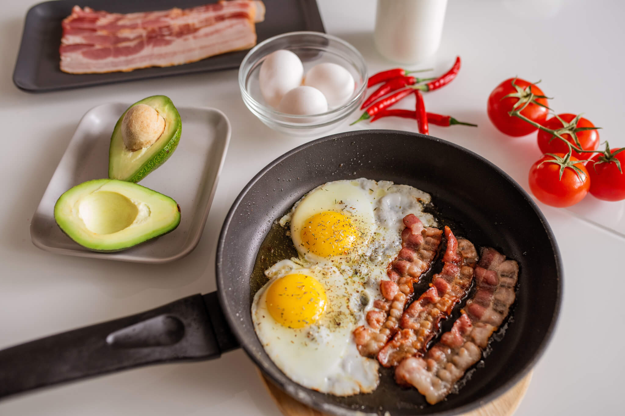 Bacon and eggs with avocado and peppers in a skillet