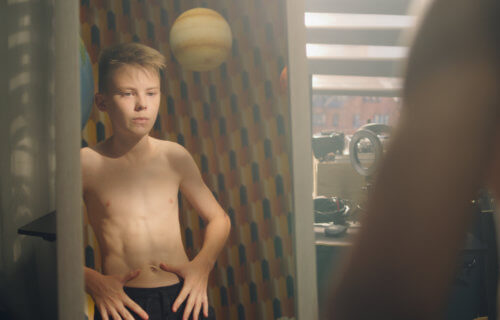 Muscular young boy examines his body infront of the mirror after weight training