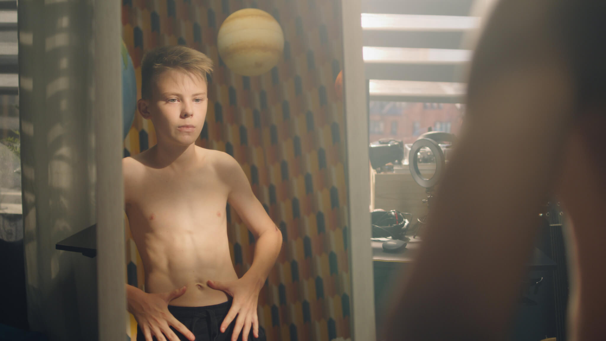 Muscular young boy examines his body infront of the mirror after weight training