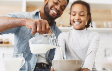 Dad pouring milk into a bowl of breakfast cereal for his daughter