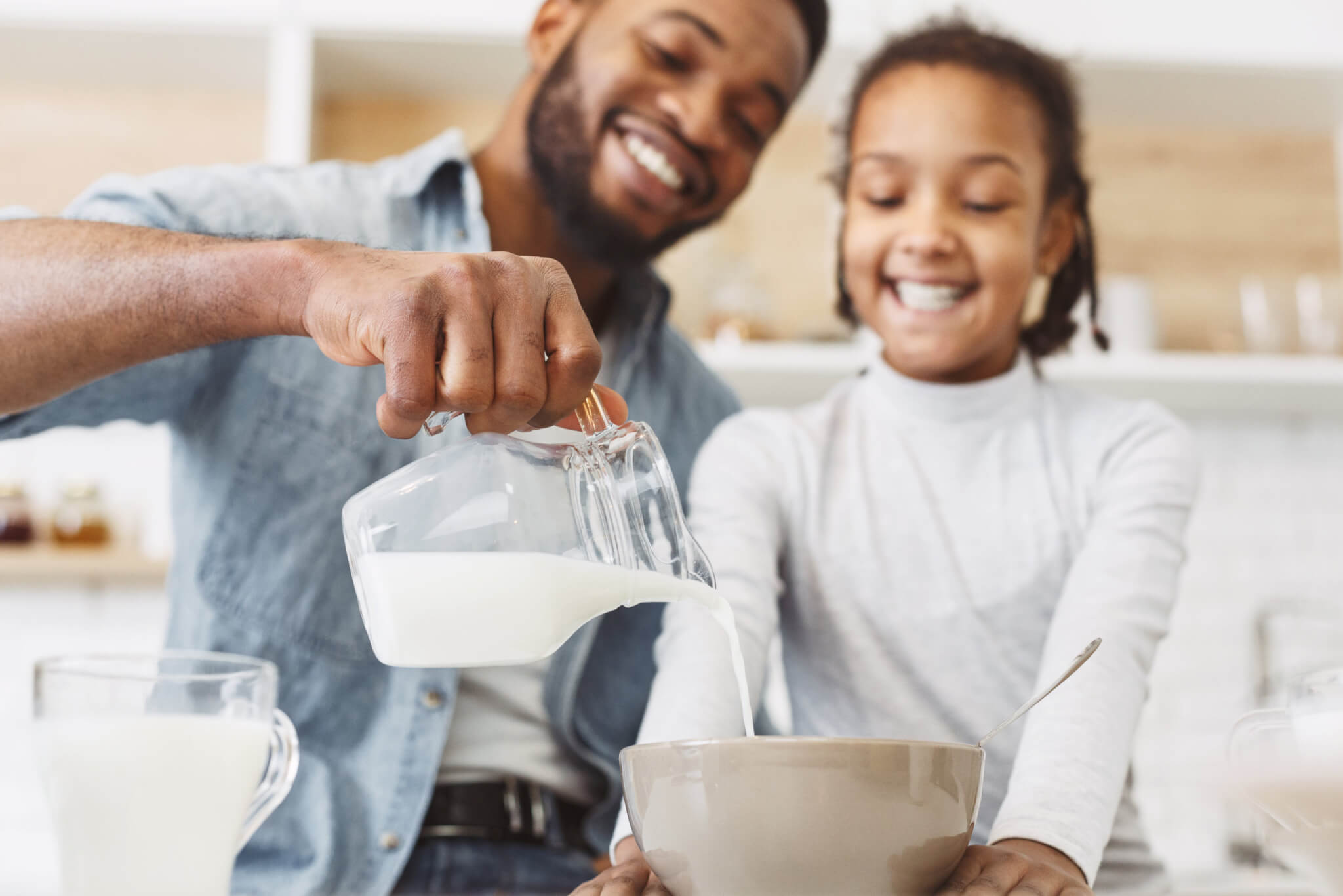 Dad pouring milk into a bowl of breakfast cereal for his daughter