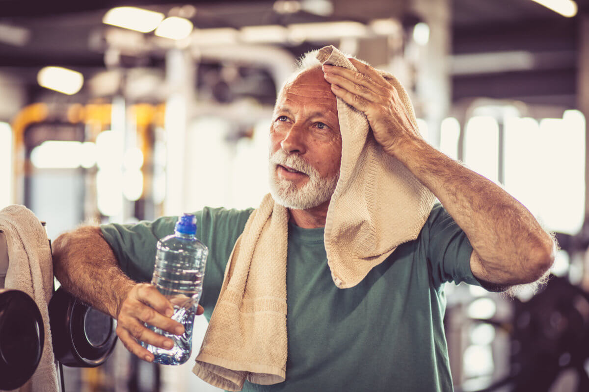 Older man wiping off the sweat from an intense exercise workout at the gym.