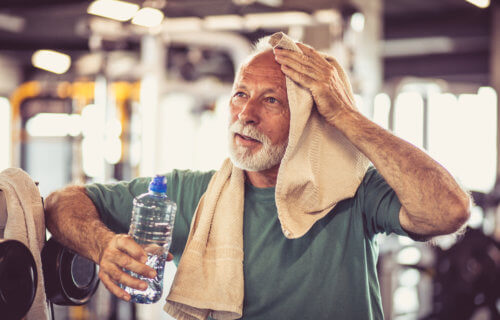 Older man wiping off the sweat from an intense exercise workout at the gym.