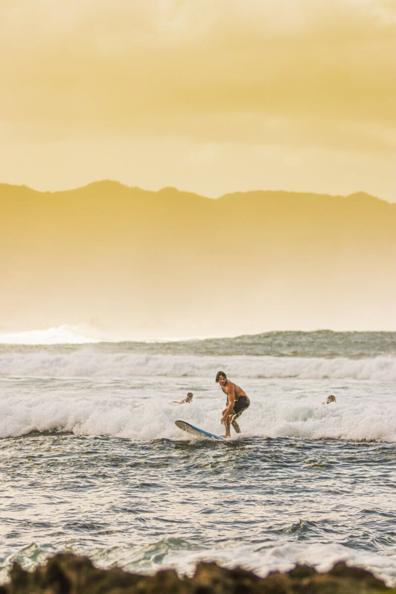 Surfer rides waves in Oahu at sunset