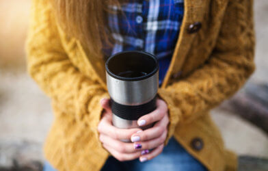 Woman holding a warm travel mug of coffee or tea in her hands