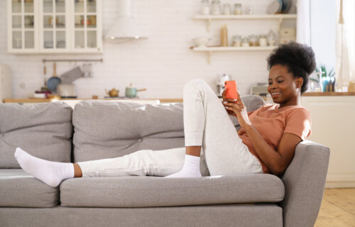 Woman relaxing on the couch in sweatpants looking at her smartphone