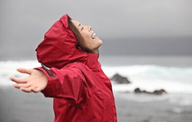 Woman wearing a rain jacket with arms outstretched at beach
