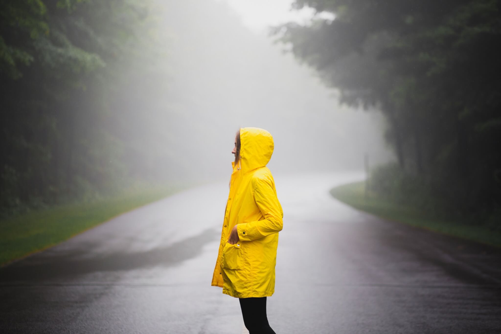 A woman in a yellow raincoat in the middle of the road.