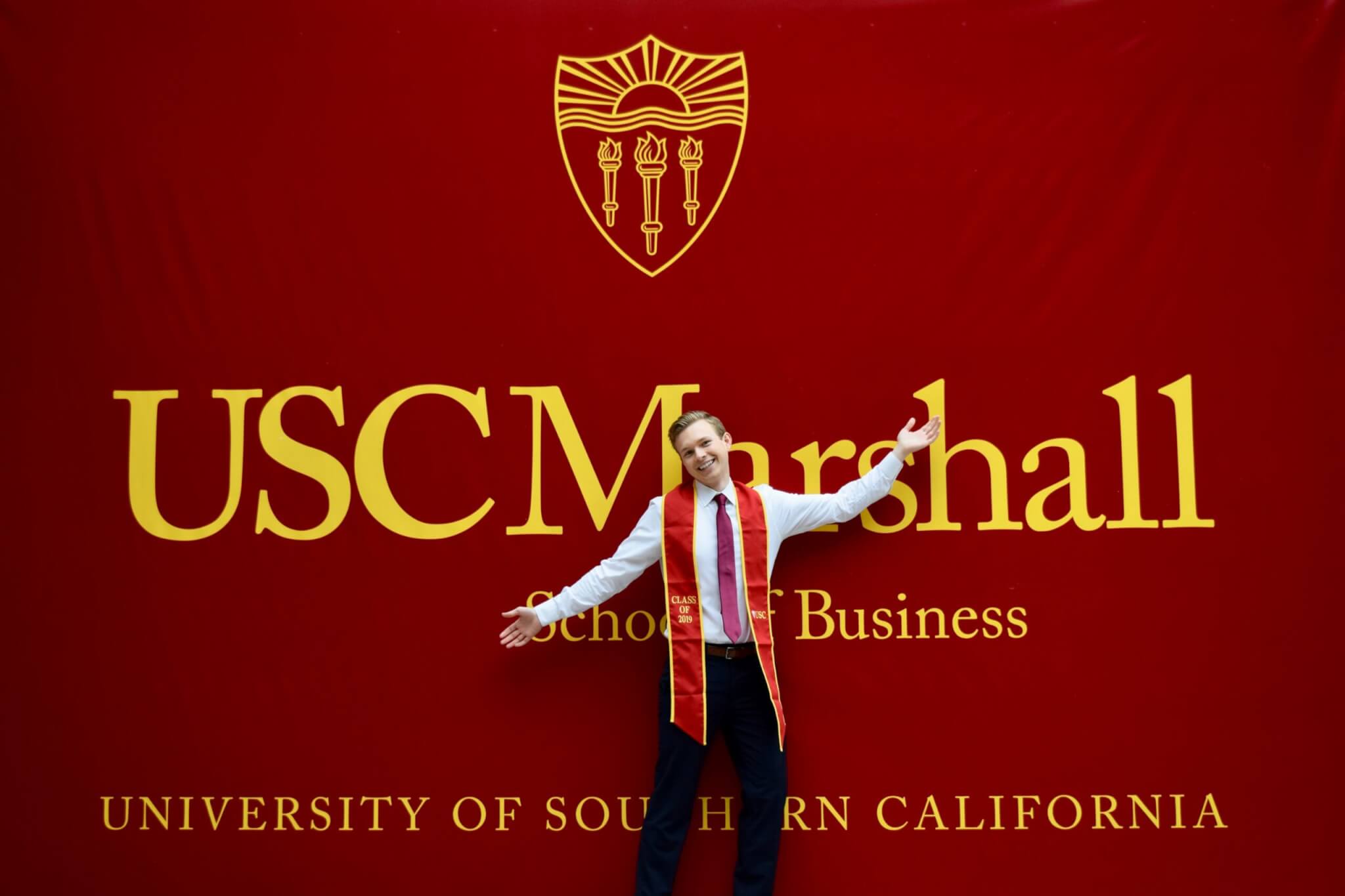 a graduate posing in front of USC Marshall banner