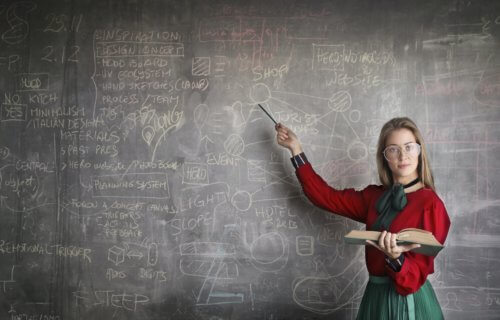 A strict teacher stands in front of a blackboard
