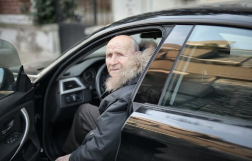 An elderly man getting into a car