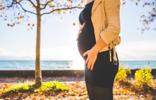 A pregnant woman standing in a park near the water