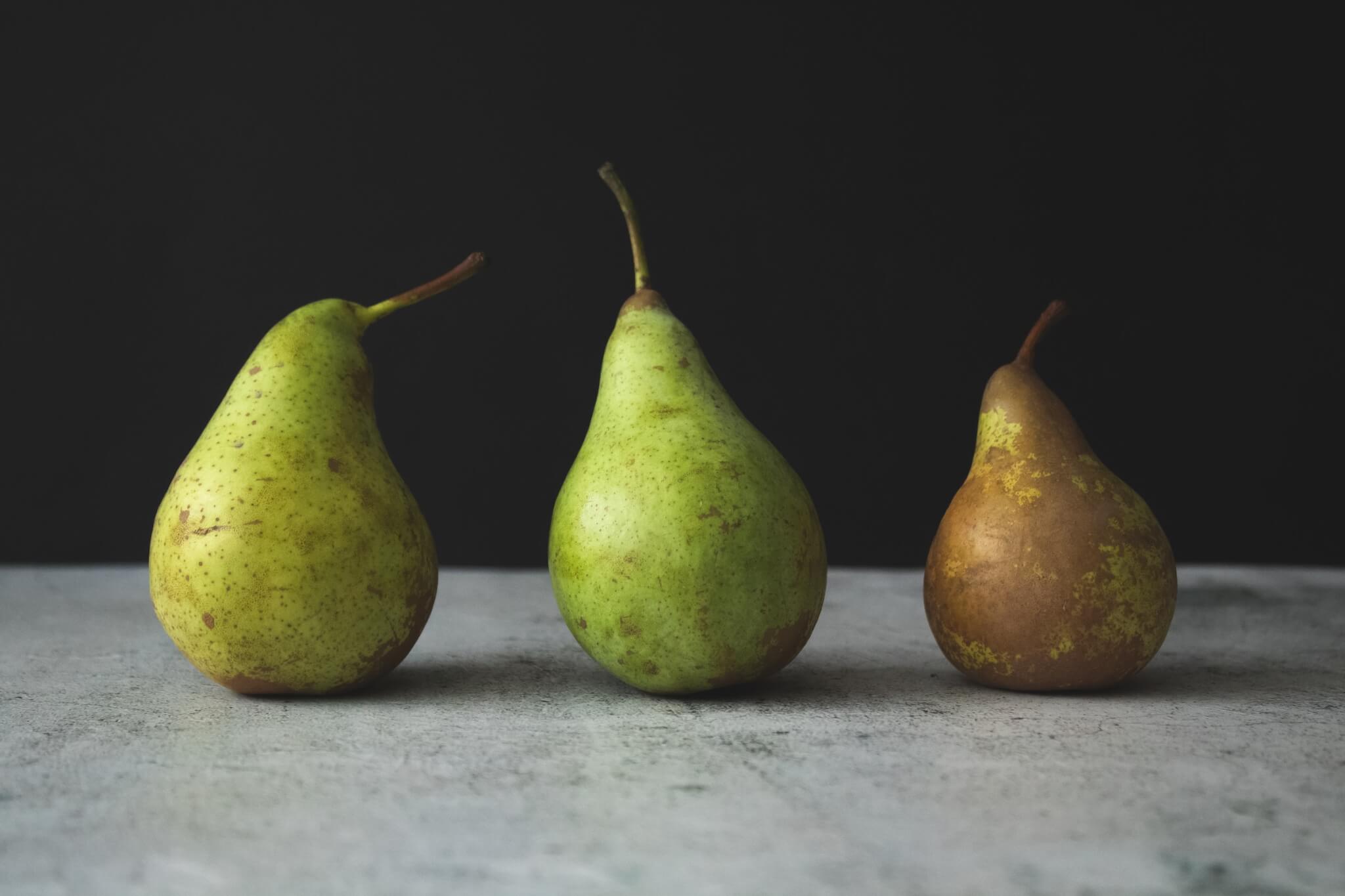 three pears in a row on a table, one brown