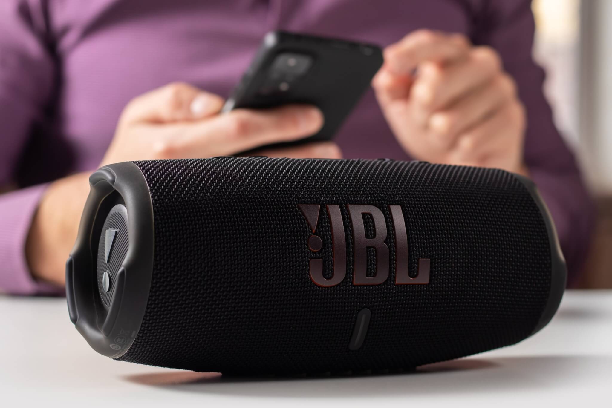 Person using JBL Charge 5 speaker with their smartphone
