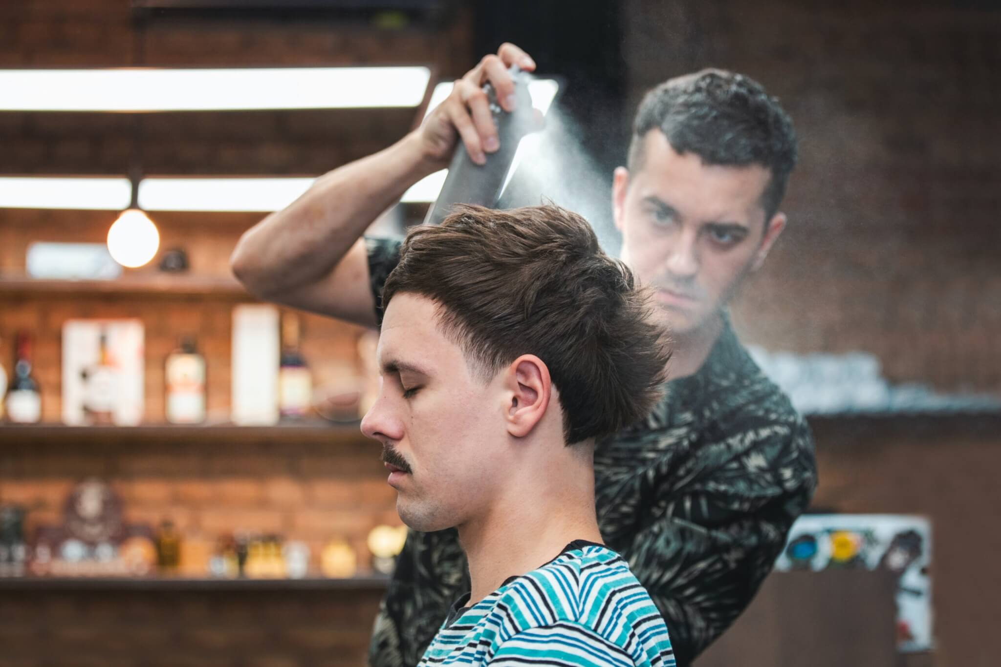 Stylist using hairspray while cutting man's hair