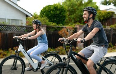 Two people smiling while riding bikes, wearing helmets