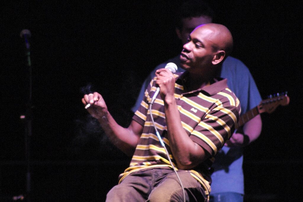 image of dave chappelle performing on stage with a microphone in his hand