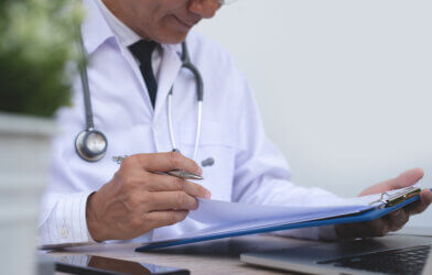 Doctor working in medical office writing notes on clipboard