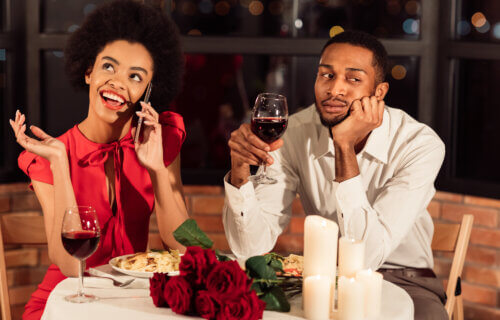 Bored man having a horrible date while woman talks on phone at dinner