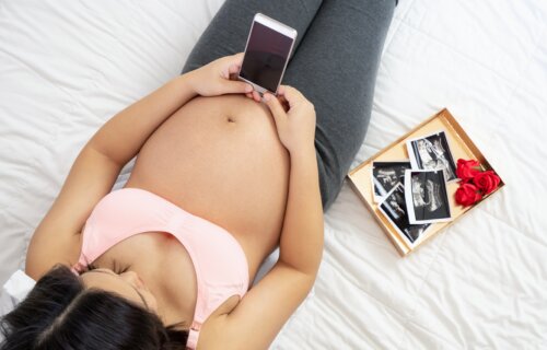 Pregnant woman looking at smartphone in bed