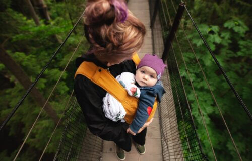 Woman carrying baby on a bridge in the forest