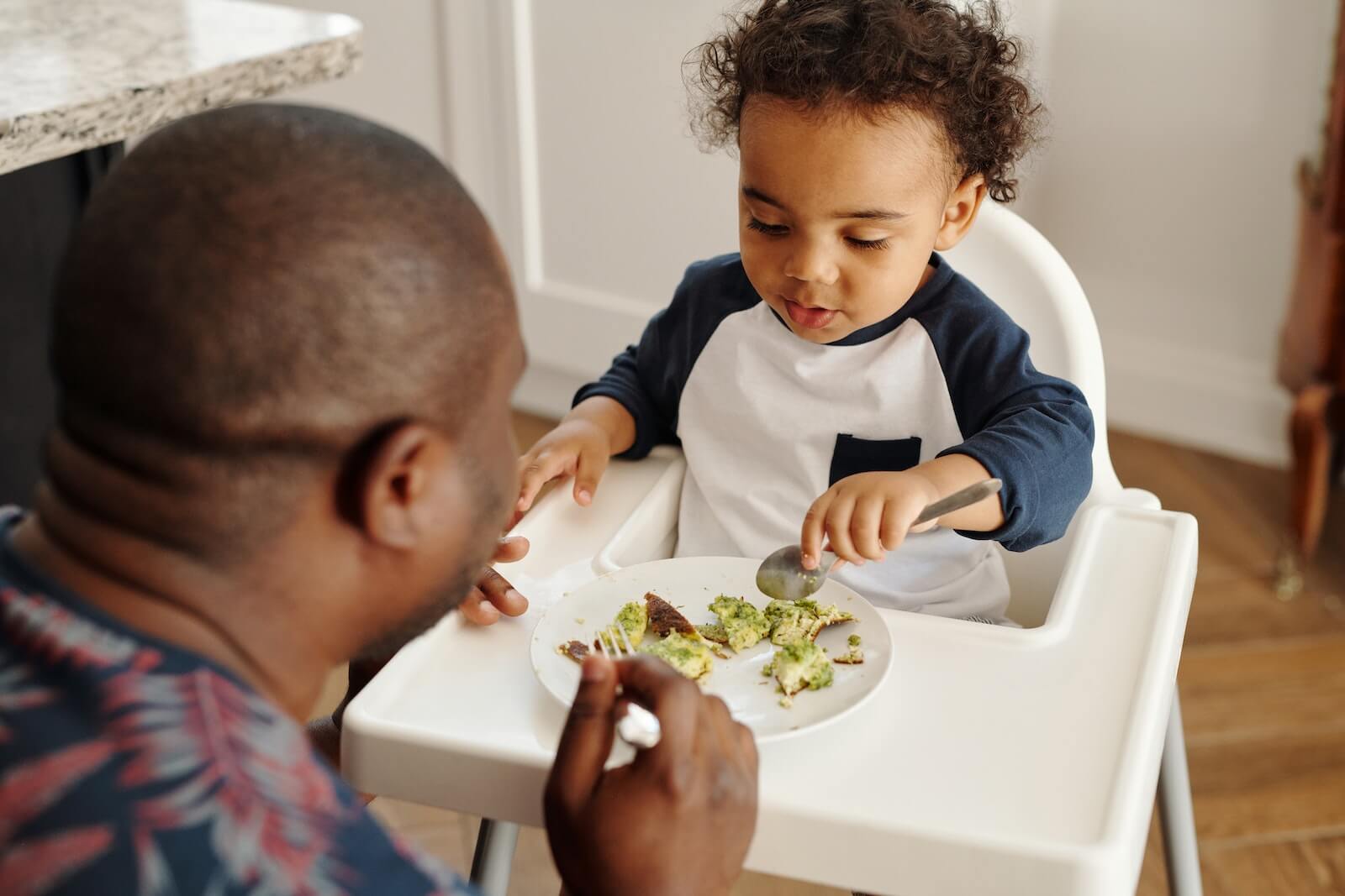 A father feeding a baby in a high chair