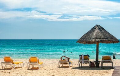 Beach chairs and umbrella in front of turquoise water on the beach in Mexico