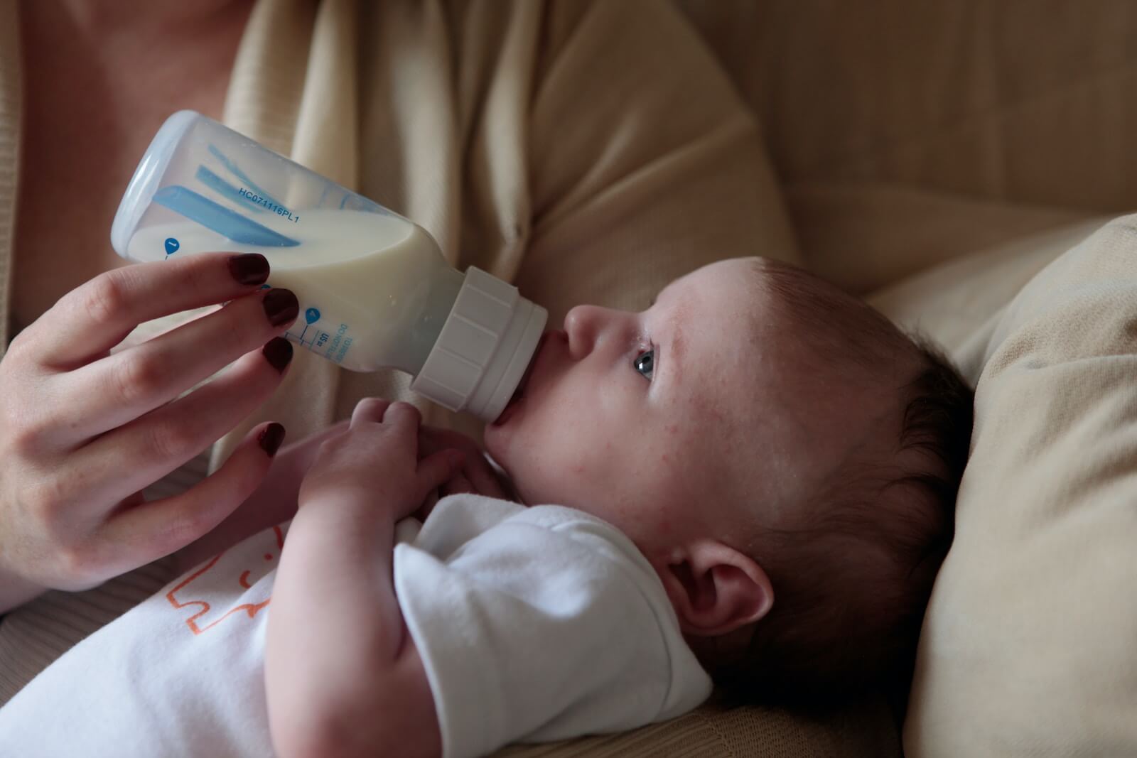 baby drinking from bottle in person's arms
